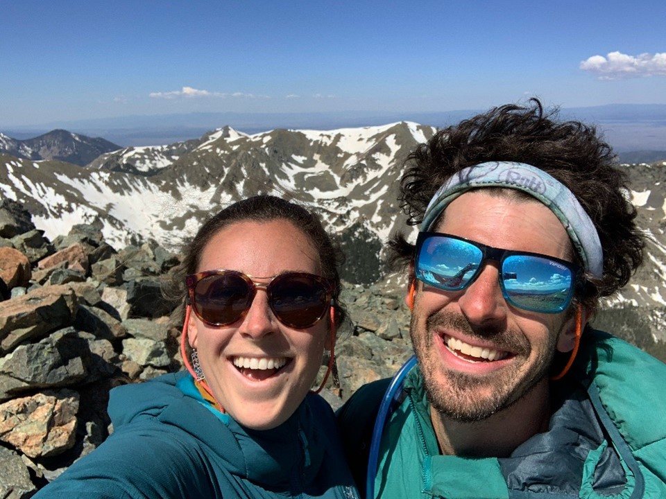A selfie photograph with snowy mountains in the background on a sunny day pictured left is Alexis Anderson and pictured right is her partner Evan