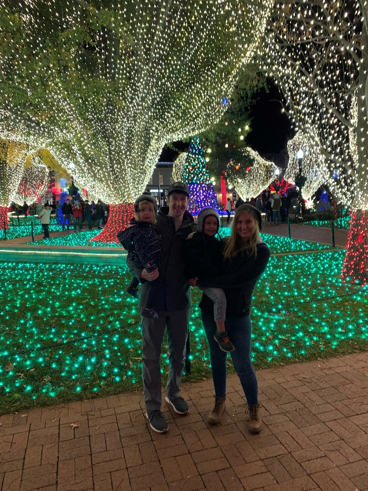 A photo of David Gardner and his family standing in front of stringed lights at an outdoor park. 