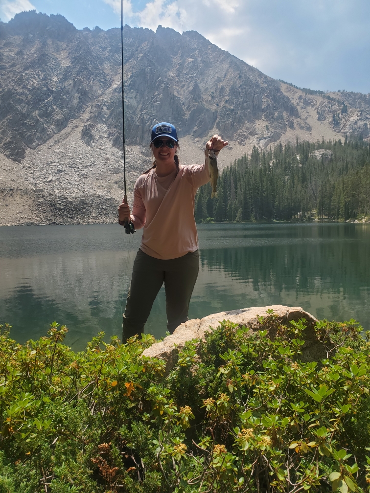 Demsie Butler showing off her recently caught fish with the lake and mountains in the background.