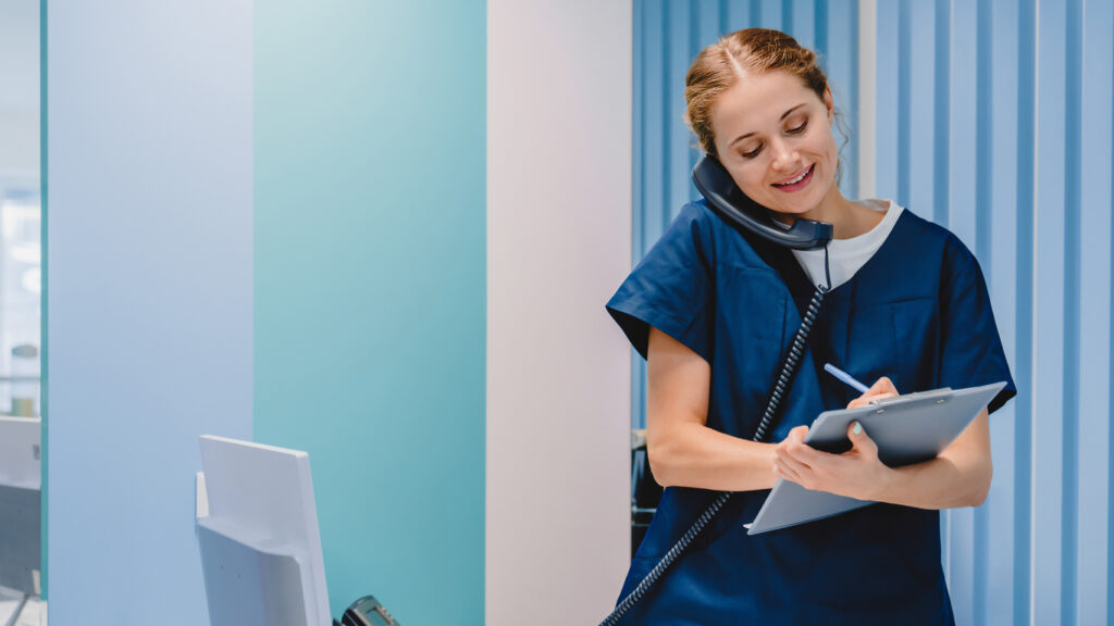 Caucasian female practitioner working at reception desk while answering phone call.