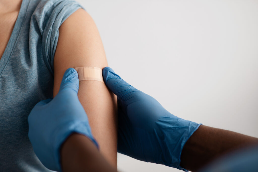 someone receiving their vaccine and a healthcare provider placing a bandage over their arm